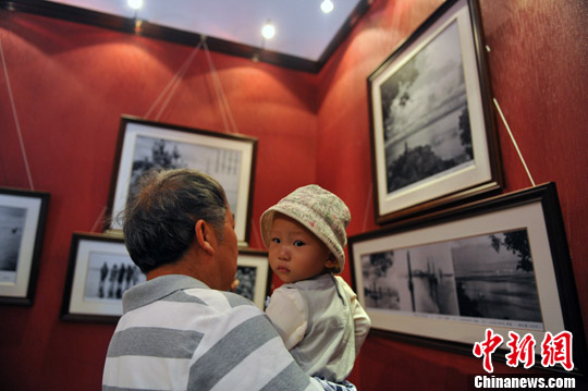 图为爷爷抱着儿孙来看展览，讲述自己年轻时的故事。中新社发 任东摄
