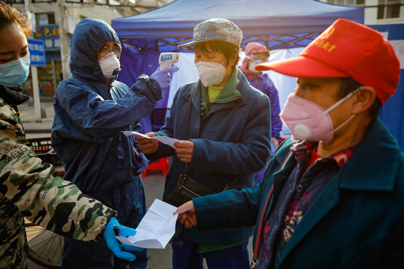　　2月22日，在武汉市百步亭社区建设新村，社区工作人员（左一、左二）在出入口查看居民进出凭证，并为居民测量体温。新华社记者 沈伯韩 摄