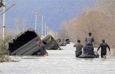 Albanian army rescuers and villagers pass by a convoy of trucks pushed to the side of the road by flood water on the outskirts of Bacallek, near the city of Shkodra, Sunday, Jan. 10, 2010. (AP Photo/Hektor Pustina)