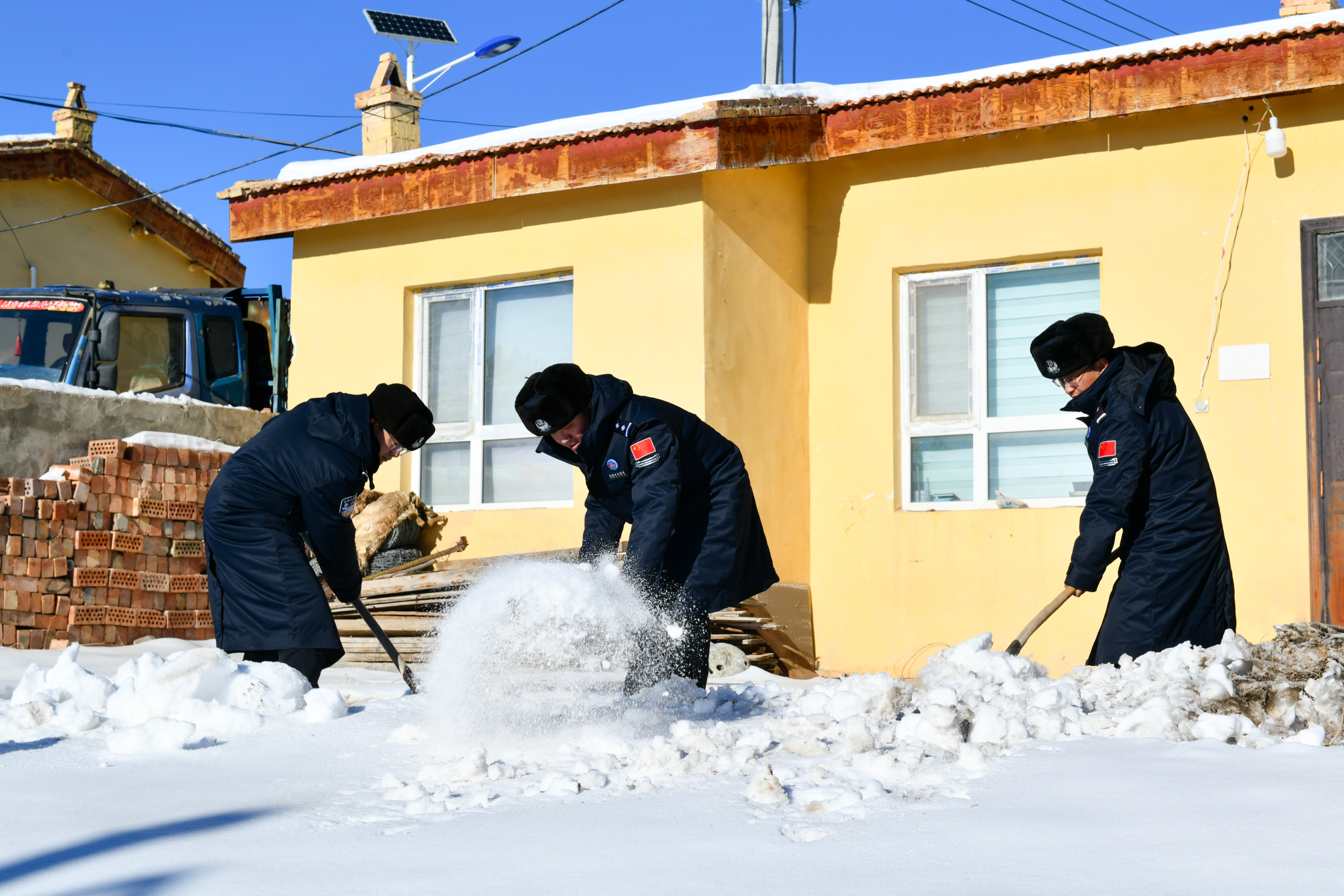 图为民警帮助托乎提汗亚热老人清理院落积雪