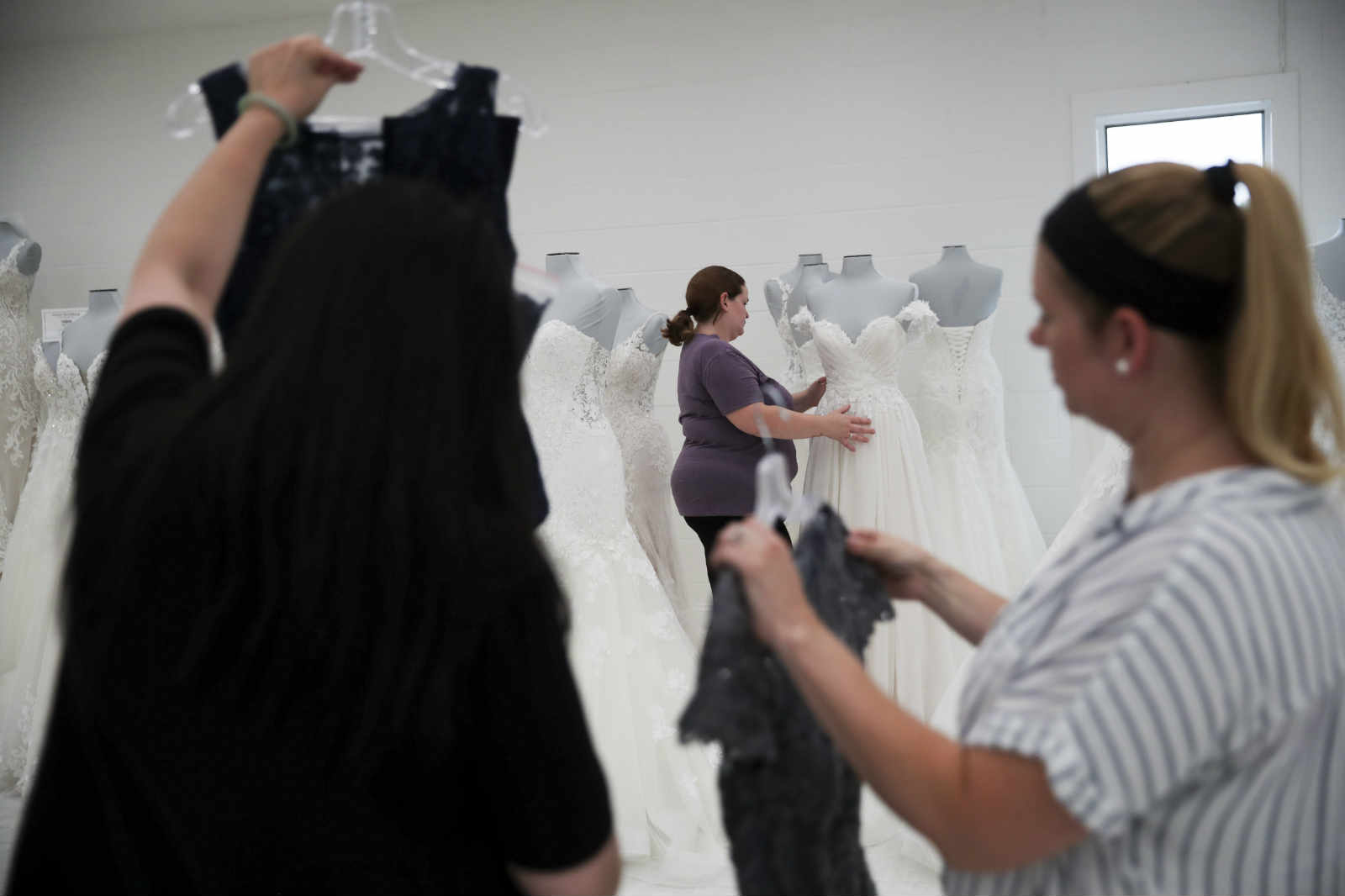 Workers settle bridal and prom dresses for display at U.S. brand Mon Cheri